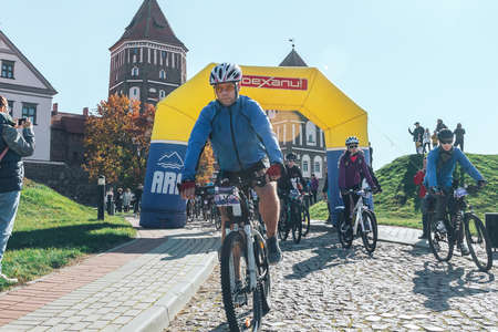 October 6, 2018 Novogrudok Belarus Castle Road There are cyclists with glasses who ride along the stone road at the beginning of the marathon in front of the castleのeditorial素材