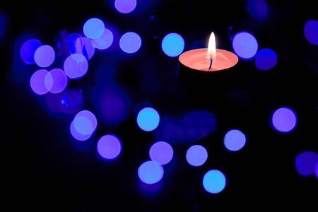 The concept of prayer and hope.The flame of a burning candle at night with a magical abstract round bokeh on the background of Christmas lights.の写真素材