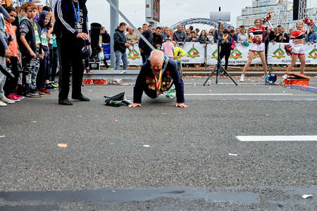 September 15, 2019 Minsk Belarus An elderly man with military medals does push-ups on the street next to dancing girlsのeditorial素材