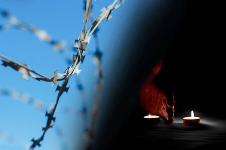 There is a human hand lit by burning candles next to the barbed wire on memorial dayの写真素材