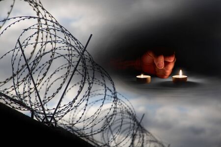 A man's fist is lit by burning candles next to barbed wire on memorial dayの写真素材
