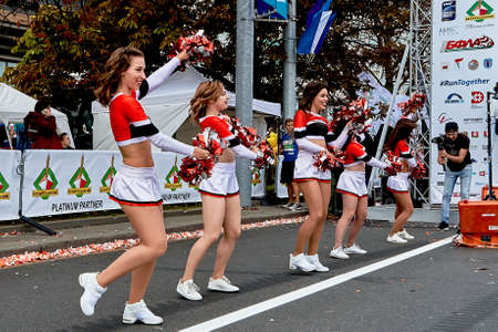 September 15, 2019 Minsk Belarus The photographer takes pictures at the start of the marathon as happy girls-dancers of support groups perform well with large bows in their hands.のeditorial素材