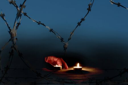 A man's fist is lit by burning candles next to barbed wire on memorial dayの写真素材