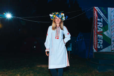 July 6-7, 2019 Village Petrevichi Minsk region Belarus Beetle trail 12 Midsummer A young woman with a wreath of flowers on her head with a microphone in her hand stands against the night backgroundのeditorial素材