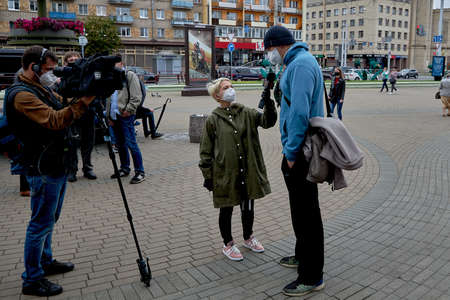 June 14 2020 Minsk Belarus A masked cameraman with a camera and a masked female reporter with a microphone talk to a tall masked man on the streetのeditorial素材