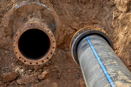 An old steel water pipe with a welded flange lies next to a new plastic pipe installed to connect the water supply systemの写真素材