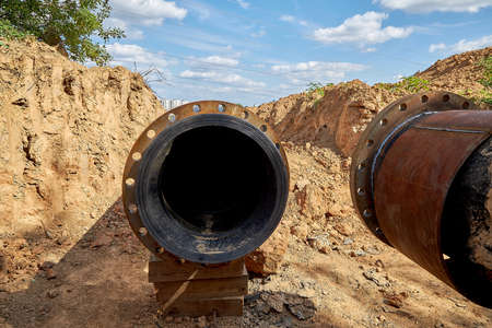 An old steel water pipe with a welded flange next to a plastic pipeの写真素材