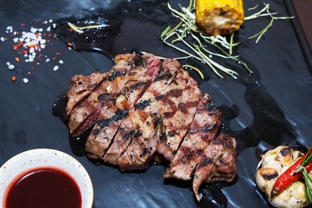 barbeque meat composition on a black background with tomato sauce, corn, rosemary and pepper. Appetizing meat roasted BBQ grillの写真素材