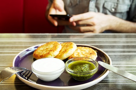 Homemade Salty Cheese Pancakes with sauce Pesto. Guy with the phone on the background. Pancakes photographed close.の写真素材