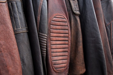 Collection of leather jackets on hangers in the shop. Many new men's leather winter jackets. Background and closeup texture of biker's leather, motorcycle jackets.の写真素材