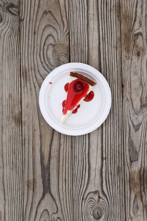 Slice of cheesecake topped with cherry compote on plate on brown table with dessert, top viewの写真素材