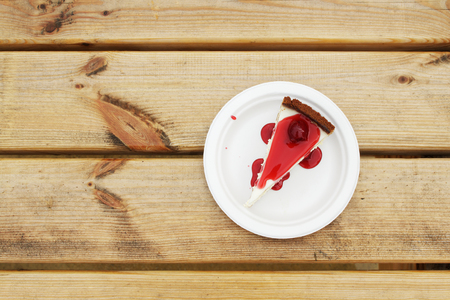 Slice of cheesecake topped with cherry compote on plate on brown table with dessert, top viewの写真素材