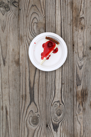 Slice of cheesecake topped with cherry compote on plate on brown table with dessert, top viewの写真素材