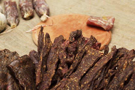 Beef jerky. Dried meat beef jerky on chopping board background. Dry meat, rustic country style. Delicious meat eating.の写真素材