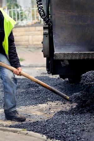 Worker manually effusing the asphalt with paving machine