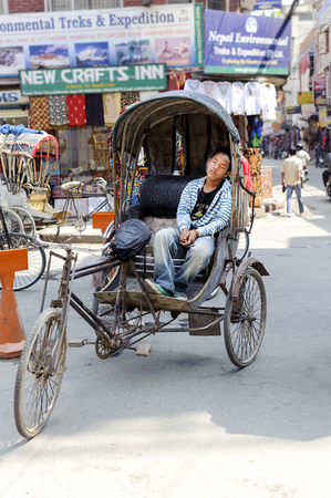 KATHMANDU, NEPAL - MAY 17, 2014: Tired cycle rickshaw driver sleeping on his vehicle at the entrance of Thamel area Kathmandu.The cycle rickshaw was built in the 1880s and was first used with regularity starting in 1929 in Singapore. Six years later they のeditorial素材
