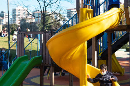 Kadikoy, Istanbul, Turkey - 02.18.2021: a child with covid mask goes down the slide and parents waiting in Freedom Park public parkのeditorial素材