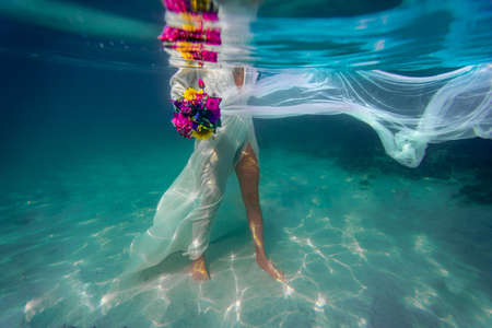 Underwater bride with flowers in a white dress in dark blue water, mediterranean seaの写真素材