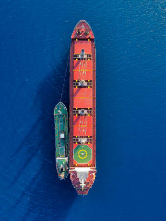 Aerial Top View of red big cargo ship with small green ship in blue smooth Mediterranean Seaの写真素材