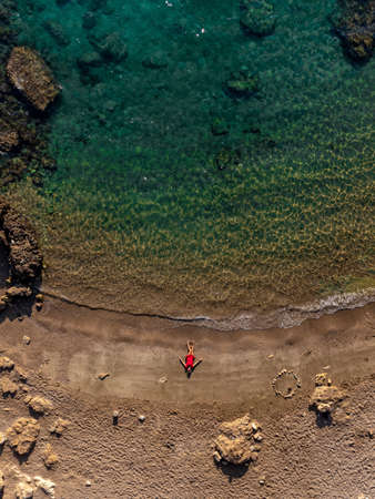 Drone Aerial Shot of girl in red dress on sandy beach, turquoise Mediterranean sea Cyprus island Vacation Holidayの写真素材