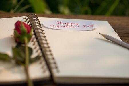 notepad and red rose on wooden backgroundの写真素材