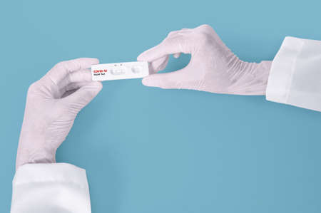 Scientist hands showing rapid laboratory COVID-19 test for diagnosis  Positive test result for the new rapidly spreading Coronavirus Covid-19 on blue background Pandemic infectious conceptの写真素材