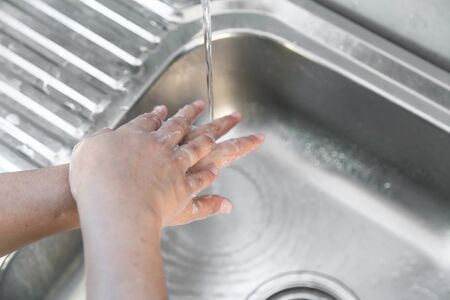 Washing hands man rinsing soap with running water at sink, Coronavirus prevention hand hygiene. Corona Virus pandemic protection by cleaning hands frequently.の写真素材