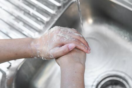 Washing hands man rinsing soap with running water at sink, Coronavirus prevention hand hygiene. Corona Virus pandemic protection by cleaning hands frequently.の写真素材