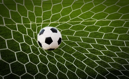 Soccer football in Goal net with green grass field の写真素材