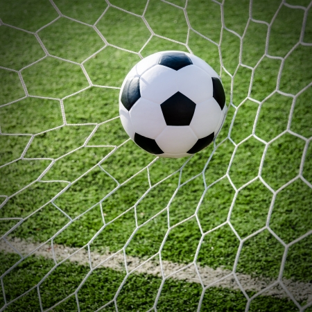 Soccer football in Goal net with green grass field の写真素材