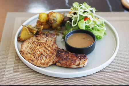 Grilled pork steak with sauce and potatoes on white plate in restaurantの写真素材