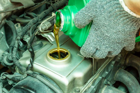 Close up of pouring new oil to old car engine.の写真素材