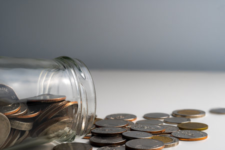 Coins in a small jar being poured on a white background