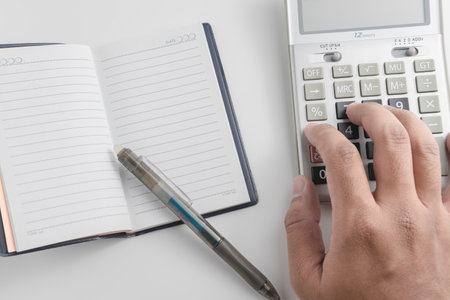 Man's hand writing on notebook with calculator and pen on white backgroundの写真素材