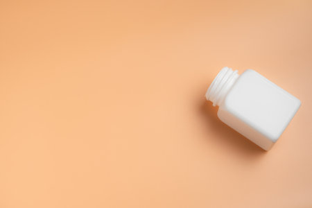 White plastic bottle on orange background. Top view with copy space.