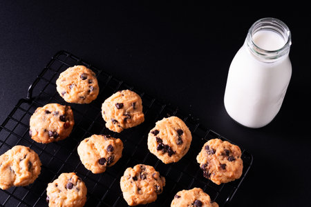 Chocolate chip cookies with a bottle of milk on a black background