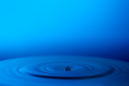 Water drop falling into water with ripples on a blue background.の写真素材