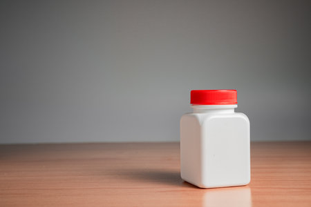 White plastic bottle with red cap on the wooden table and grey backgroundの写真素材