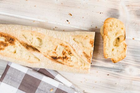 Loaf of bread with a cutted slice of bread on a wooden table. Some breadcrumbs and a towel.