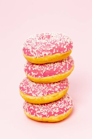 A pile of donuts in a pink glaze with a white sprinkles on a pink background. Sweets and desserts. Minimalistic background with clean place for the inscription. Copy space.の写真素材