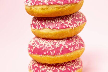 A pile of donuts in a pink glaze with a white sprinkles on a pink background. Sweets and desserts. Minimalistic background with clean place for the inscription. Copy space.の写真素材