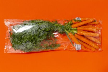 Use less plastic! Carrots in plastic packaging isolated on orange ground. Symbol for environmental pollution done by the food industryの写真素材