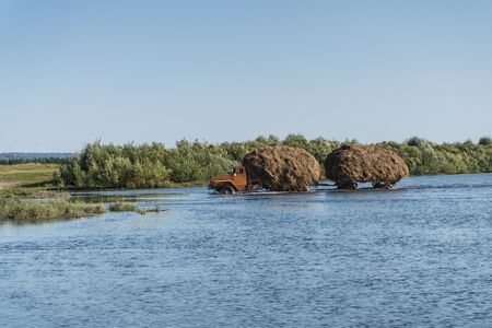 A truck with a trailer carries hay through the riverの写真素材