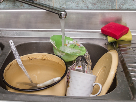 dirty dishes in a sink under running waterの写真素材