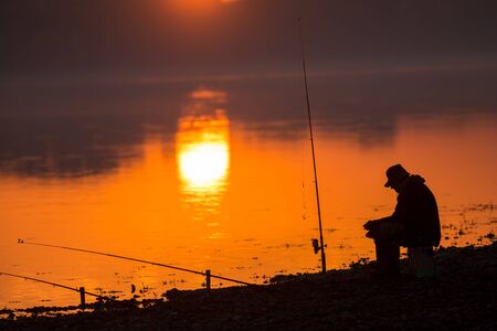 Silhouette of the fisher on a background of an evening dawnの写真素材