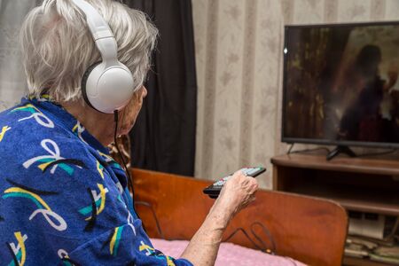 A very old woman with headphones is watching TVの写真素材
