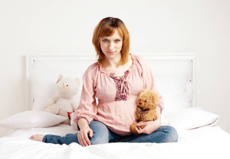The smiling beautiful pregnant woman sits on a bedの写真素材