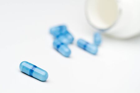 Blue capsules in front of pill bottle