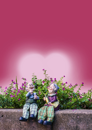 Two dolls which made like grand mom   grand dad sit on a brick wall infront of flowers and red heart back groundの写真素材
