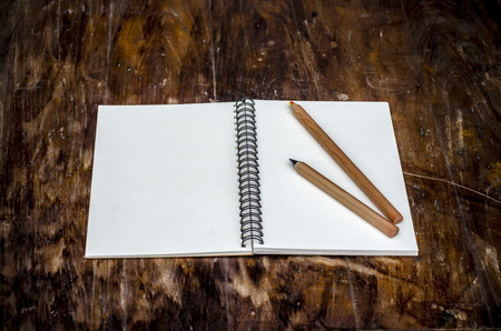 A white blank note book and pencils for your message place on old color full tableの写真素材
